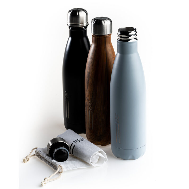 Zdjęcie: Na białym tle trzy butelki temiczne. Butelki są w różnych wariantach kolorystycznych: czarnym, drewnianym i szarym. Przed nimi zwinięty, bawełniany woreczek i korek od szarej butelki.