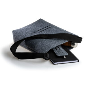 Zdjęcie: Na białym tle położona filcowa troba. Z jej środka wystaje butelka termiczna, czarny notes i etui na ołówek.